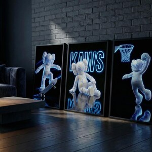 May include: Three framed art prints featuring KAWS characters in a dark room. One print shows a character on a skateboard, another shows the KAWS logo, and the third shows a character playing basketball. The prints have a neon blue glow.