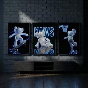 May include: Three framed art prints featuring a cartoon character in neon blue. One print shows the character skateboarding, another shows the word "KAWS", and the third shows the character playing basketball. The prints are displayed above a wooden cabinet.