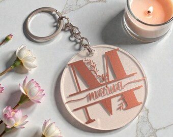 Op de afbeelding: Een heldere acryl sleutelhanger met een roségouden letter "M" ontwerp, de naam "Maria" in cursief en de letters "I" en "V" eronder. De sleutelhanger is bevestigd aan een zilveren sleutelring.