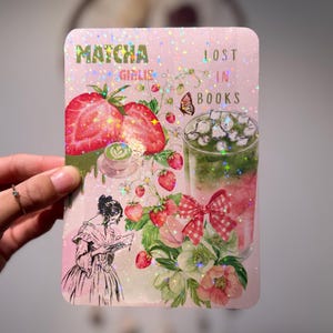 Pode incluir: Um autocolante retangular rosa com as palavras "Matcha Girlies Lost in Books". O autocolante apresenta ilustrações de morangos, uma bebida de matcha, flores e uma mulher a ler. O design tem um efeito holográfico brilhante.