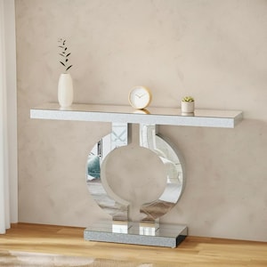 May include: A mirrored console table with a silver glitter finish. The table features a circular design in the center and a rectangular top. A white vase, a small clock, and a potted plant are displayed on the table.