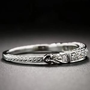 Könnte beinhalten: Ein silberner Ring mit filigranem Design. Der Ring hat eine Reihe kleiner, klarer Steine, die in einer rechteckigen Form gesetzt sind. Das Band hat ein aufwendiges, graviertes Muster. Der Ring wird vor dunklem Hintergrund gezeigt.