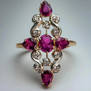 May include: A gold ring with a central oval ruby, surrounded by pear-shaped and round rubies, and accented with small diamonds. The ring has an ornate, symmetrical design with a vintage aesthetic.