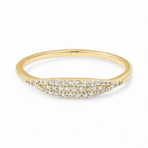 Peut inclure: Une bague dorée avec un design incurvé. La bague est ornée d'une rangée de petits pierres précieuses claires le long de la section incurvée. La bague est sur fond blanc.
