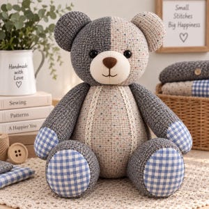 May include: A stuffed teddy bear featuring a split-color design with dark gray textured fabric on one side and light beige speckled fabric on the other. It has a cream-colored muzzle, a brown nose, and blue and white gingham patches on its feet.