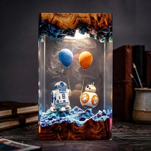 Peut inclure: Une lampe rectangulaire en résine avec une base et un sommet en bois naturel et un centre en résine époxy bleue. À l'intérieur, des figurines R2-D2 et BB-8 sur un paysage bleu texturé, tenant chacune un ballon bleu ou orange, éclairées.