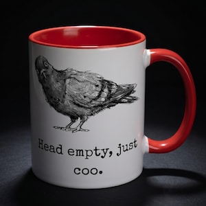 May include: White ceramic mug with a red interior and handle. The mug features a black and white illustration of a pigeon and the text "Head empty, just coo."