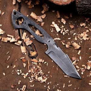 May include: A handcrafted, gray metal knife with a unique, open-handled design. The blade is straight-edged and angled, with a sharp point. The knife is shown on a wooden surface with wood shavings.