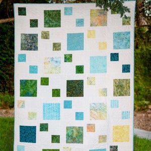 May include: A white quilt with a scattered pattern of colorful squares in shades of green, blue, and yellow. The quilt is designed with 5-inch and 10-inch squares. The text "pebble path" and "A pattern for 5" and 10" squares" are visible.