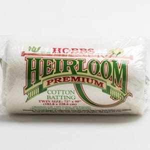 May include: A roll of Hobbs Heirloom Premium Cotton Batting in a clear plastic bag. The label features green and red text, stating the twin size is 72" x 90". The batting is made of 80% cotton and 20% polyester.