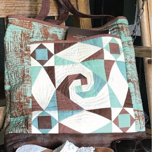 May include: A brown and turquoise patchwork tote bag with a geometric design. The bag has a large pocket on the front with a spiral pattern. The bag is sitting on a wooden surface with a pair of white sandals and sunglasses.