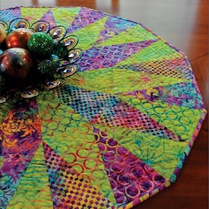 May include: A colorful, quilted table runner with a geometric design. The runner features vibrant green, purple, and yellow patterns. The text "Over Under" and "Swirly Girls" are visible. The runner is designed for use on a table or under a tree.