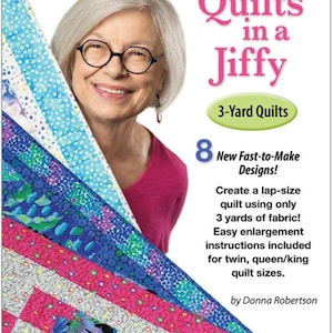 May include: A book cover with a woman smiling and holding a stack of colorful fabric squares. The title is "Quilts in a Jiffy" and the subtitle is "3-Yard Quilts". The book features 8 new fast-to-make designs and instructions for making lap-size quilts using only 3 yards of fabric.