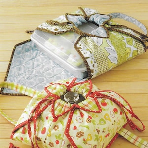 May include: A quilted fabric lunch bag with a clear plastic container inside, and a matching drawstring bag with red polka dot trim. The bags are decorated with fruit and floral patterns. The text "Atkinson Designs" and "Hot Stuff!" are visible.