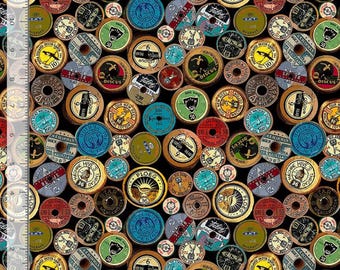 May include: A black fabric featuring a repeating pattern of vintage wooden thread spools in various colors including yellow, blue, green, and red. Each spool displays unique brand labels and text. A ruler showing 11 inches is visible on the left.