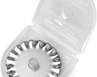 May include: A circular stainless steel rotary cutter blade with a scalloped edge, featuring the embossed text OLFA STAINLESS JAPAN. The blade is housed inside a clear, hinged plastic storage case with molded text on the interior lid.
