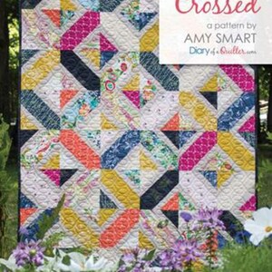 May include: A colorful quilt with a geometric pattern. The quilt features a mix of triangles and rectangles in various colors, including pink, yellow, blue, and orange. The text "Double Crossed" is displayed on a white background.
