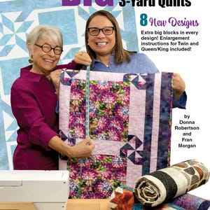 May include: A Fabric Cafe book cover titled "BIG BLOCK 3-Yard Quilts" featuring two women holding a floral quilt. The cover includes text about new designs and enlargement instructions. Rolled quilts and sewing supplies are also visible.