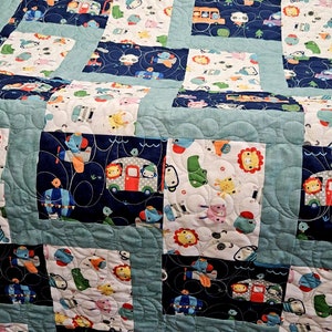 May include: A blue and white baby quilt with a patchwork design featuring various animals and vehicles. The quilt is made of soft cotton fabric and is perfect for a nursery or playroom.
