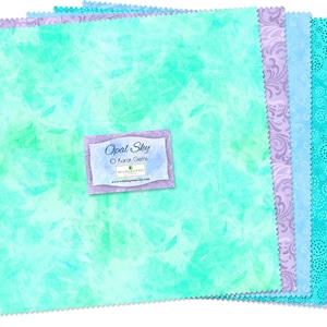 May include: A stack of square fabric swatches in shades of turquoise, teal, and lavender with various patterns including marble, floral swirls, and dots. A rectangular label on top reads Opal Sky 10 Karat Gems Wilmington Prints with a website URL.