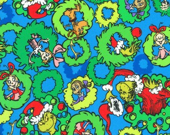 May include: A blue fabric featuring a repeating pattern of bright green Christmas wreaths. Each wreath contains a character from the Grinch story, including the Grinch wearing a red Santa hat, Max the dog, and various Whos, accented with red ornaments.