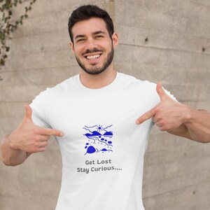 May include: White t-shirt featuring a blue landscape graphic and the text "Get Lost Stay Curious...." A person is pointing at the shirt.