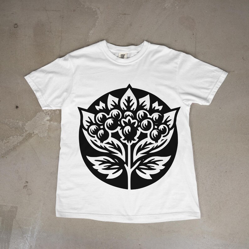 May include: A white short-sleeve t-shirt featuring a large, circular black graphic print on the chest. The design depicts a stylized botanical illustration of a plant with rounded berries, pointed leaves, and serrated foliage elements.