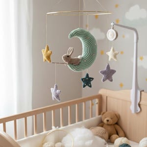 May include: A handmade baby mobile featuring a crocheted crescent moon with a bunny, and hanging stars in yellow, purple, and blue. The mobile is suspended above a wooden crib, creating a whimsical nursery decor.