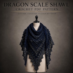 Puede incluir: Un chal de ganchillo azul marino oscuro con un patrón texturizado de escamas de dragón drapeado sobre un maniquí. El texto DRAGON SCALE SHAWL CROCHET PDF PATTERN GOTHIC FANTASY CALYXO SHOP aparece en letras blancas en la parte superior.