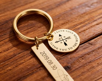 May include: Gold-colored keychain with a round charm and a rectangular tag. The round charm has a compass design and the text "I love you to the moon". The rectangular tag displays the date "2019.08.30" and a map.