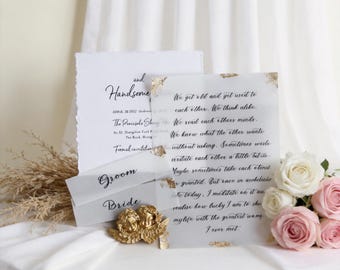 Könnte beinhalten: Ein Hochzeitspapeterie-Set bestehend aus einer weißen Einladung mit Büttenrand, einem transparenten Pergament-Overlay mit schwarzer Kalligrafie, zwei kleinen weißen Karten mit der Aufschrift Groom und Bride, einem goldenen Putto und rosa und weißen Rosen.
