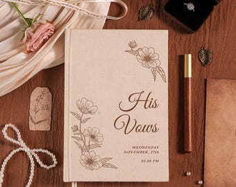 May include: A beige wedding vow book with floral illustrations and the words "His Vows" in brown script. The date "Wednesday, November 27th, 05.00 PM" is printed below. A ring box, pen, and pearls are also visible.