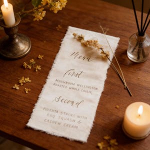 May include: A rustic menu card with handwritten text, featuring "Menu", "First", and "Second" headings, with dish descriptions. The card is on a wooden table, decorated with candles, flowers, and a diffuser.