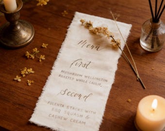 May include: A rustic menu card with handwritten text, featuring "Menu", "First", and "Second" headings, with dish descriptions. The card is on a wooden table, decorated with candles, flowers, and a diffuser.