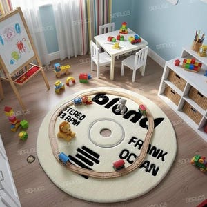 May include: A cream-colored, round rug designed to resemble a vinyl record, with the text "FRANK OCEAN" and "blond" printed on it. A toy train circles the rug, with a small lion and teddy bear. The rug is in a child's playroom.