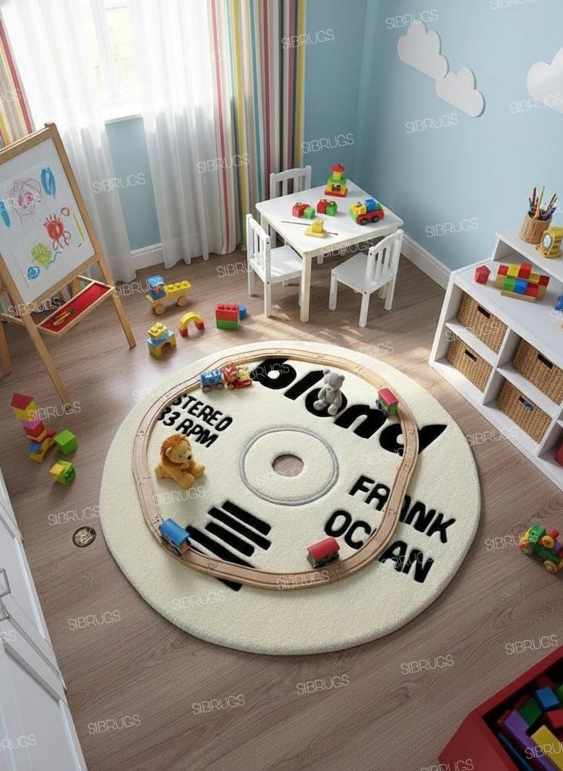 May include: A cream-colored, round rug designed to resemble a vinyl record, with the text "FRANK OCEAN" and "blond" printed on it. A toy train circles the rug, with a small lion and teddy bear. The rug is in a child's playroom.