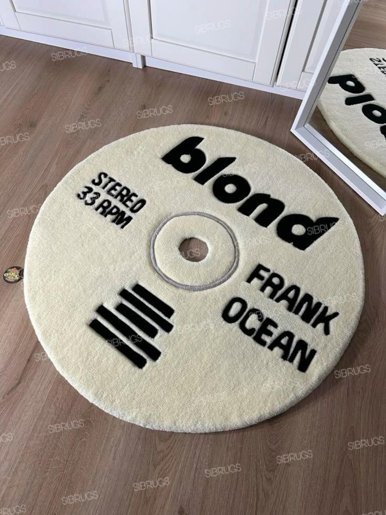 May include: A cream-colored, circular rug with black text that reads "blond", "STEREO 33 RPM", and "FRANK OCEAN". The rug is designed to resemble a vinyl record.
