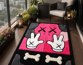 Puede incluir: Una alfombra rectangular con un diseño vibrante en rosa y negro, que incluye guantes blancos estilo caricatura, ojos en forma de cruz y dos detalles con forma de hueso. La alfombra tiene una superficie texturizada y afelpada.