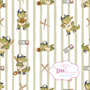 Peut inclure: Un motif répétitif avec des crocodiles de dessin animé portant des uniformes et casquettes de baseball, des battes, des balles et des billets sur un fond blanc à rayures beiges verticales. Un logo rose en forme de nuage indique Kara Lane corner.