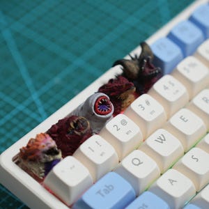 Pode incluir: Uma caneca de cerâmica branca com uma alça preta e o texto "But first, coffee" em estilo manuscrito. A caneca está sobre uma superfície branca. A caneca tem 10 cm de altura.