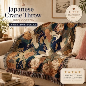 Può includere: Una coperta giapponese con gru, 100% cotone, drappeggiata su un divano. La coperta presenta uno sfondo blu navy con gru bianche, motivi floreali e un bordo con frange. Il testo recita "Woven, Soft, Durable."