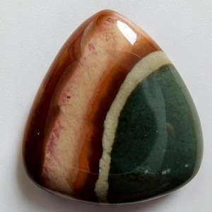 May include: Polished gemstone with a triangular shape. The stone features bands of color, including shades of brown, cream, white, and dark green. The surface is smooth and glossy, reflecting light.