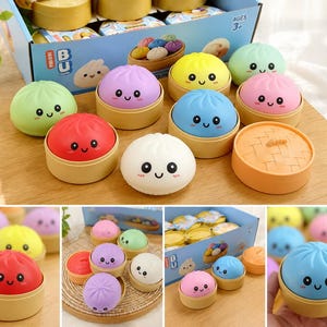 Peut inclure: Ensemble de jouets en forme de raviolis souriants, aux couleurs vives : vert, rouge, jaune et bleu, chacun dans un contenant en forme de panier en bambou. Les jouets sont présentés dans une boîte avec le mot "BU".