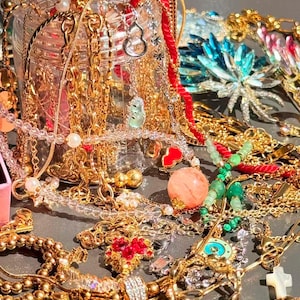 以下が含まれることがあります： さまざまなチャームとペンダントが付いた、金のネックレス、ブレスレット、イヤリングのコレクション。ジュエリーには、パール、宝石、赤いアクセントが含まれています。一部の作品はガラス瓶に展示されています。