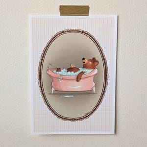 May include: An illustration of a brown bear relaxing in a pink bathtub filled with bubbles. A small yellow rubber duck floats nearby. The artwork is framed within an oval border on a patterned background.