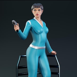 May include: A figurine of a person with short dark hair wearing a bright blue long-sleeved jumpsuit with white collar accents and a silver belt. The figure holds a small silver handheld device in one hand and stands behind a black metal frame.
