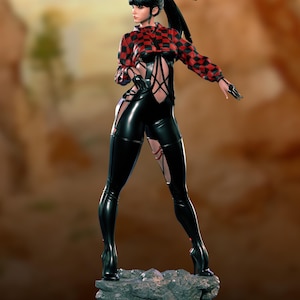 May include: A figurine of a woman in a black and red checkered top and black latex-like trousers and boots. The figure is standing on a rock with a blurred background. The woman has black hair and is wearing gloves.