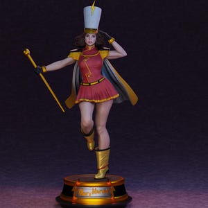 May include: A figurine of a character wearing a red and gold marching band uniform with a tall white hat featuring a yellow lightning bolt. The figure holds a gold baton, wears a cape, and stands on a circular base with the text Mary Marvel.