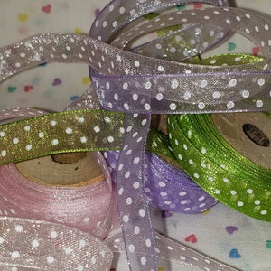 May include: Three spools of sheer ribbon with white polka dots. The ribbons are pink, lavender, and green.