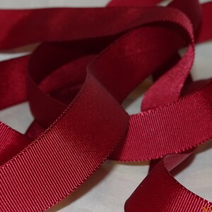 Könnte beinhalten: Nahaufnahme eines Spulens mit tiefrotem Grosgrainband. Das Band hat einen dezenten Glanz und eine gerippte Textur.
